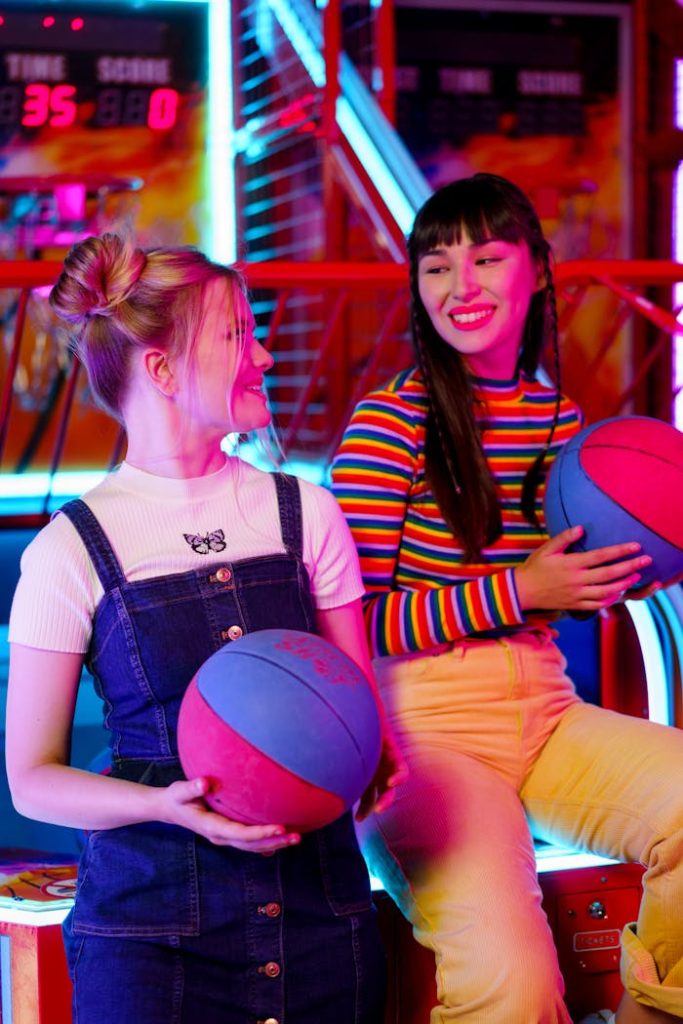 Two young women enjoying a colorful gaming experience at an amusement arcade.